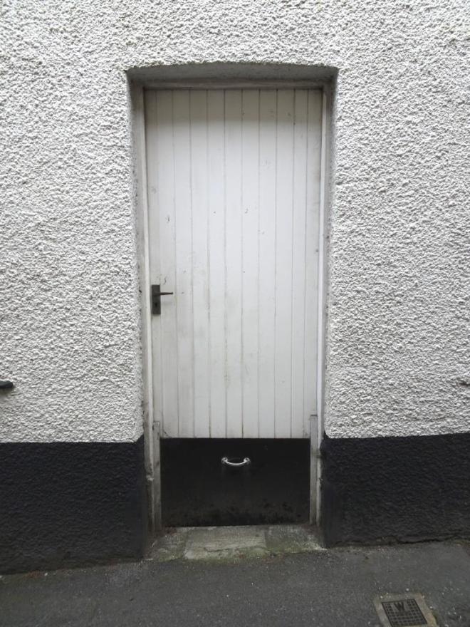 White door with a small black flood gate slotted in at the bottom, Fowey, Cornwall, September 2019