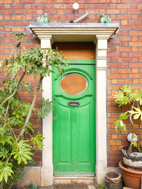 Green door with dragons and a lump hammer on the cornice, Greenbank, Bristol, February 2023