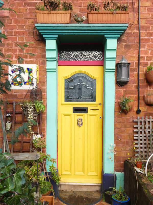 Yellow door wirh a dodo and planters on the cornice, Greenbank, Bristol, February 2023