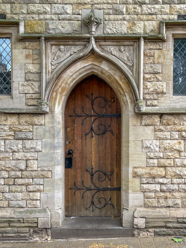 Fine stonework surrounds a door with fancy hinges, Lincoln, June 2023