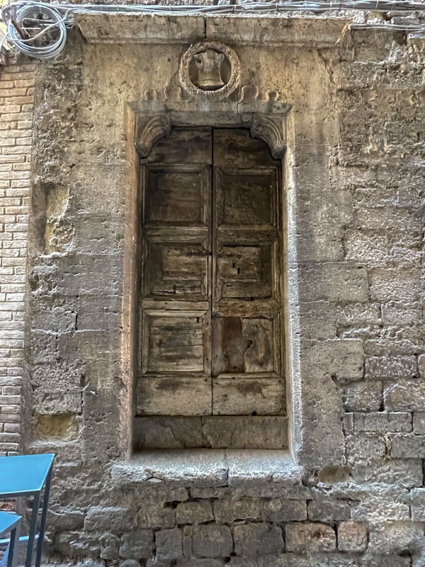 Wonderful old door perched on a wall with a wreath crest, Perugia, Umbria, Italy, July 2023