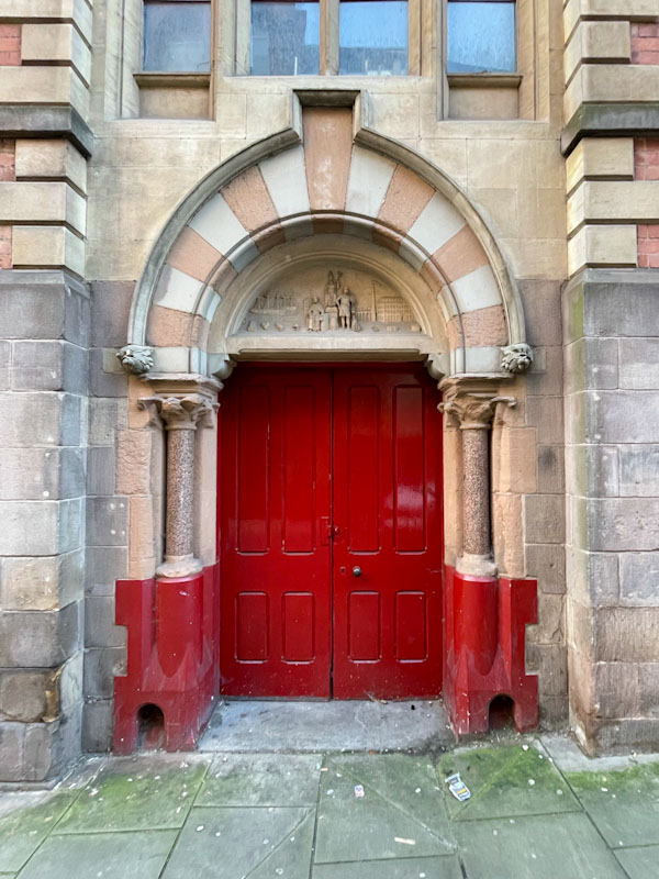 Red doors, a beautiful stone arch and boot scrapers on either side, Nottingham, November 2023
