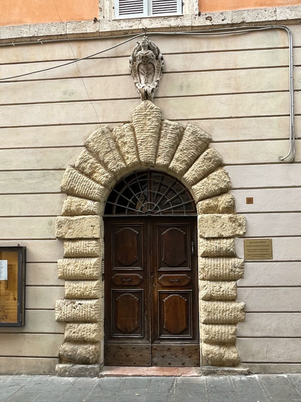 Arch surround and crest, with fan light and wooden door, Assisi, Umbria, Italy, July 2023