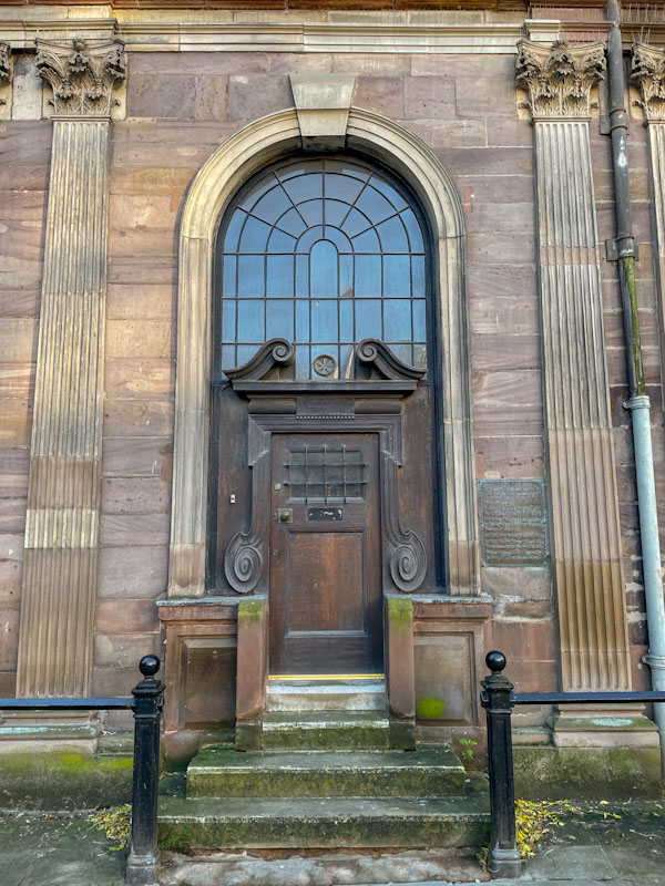 Ornate wooden scrolls and steps up to this door within an archway, Manchester, November 2023
