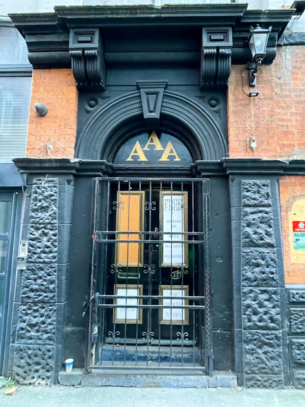 Grand doorway, security gate and black door with notice panels, Manchester, November 2023