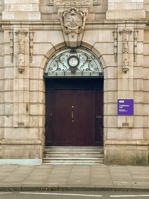 Fancy stonework and ironwork around a fairly utilitarian door, Manchester, November 2023