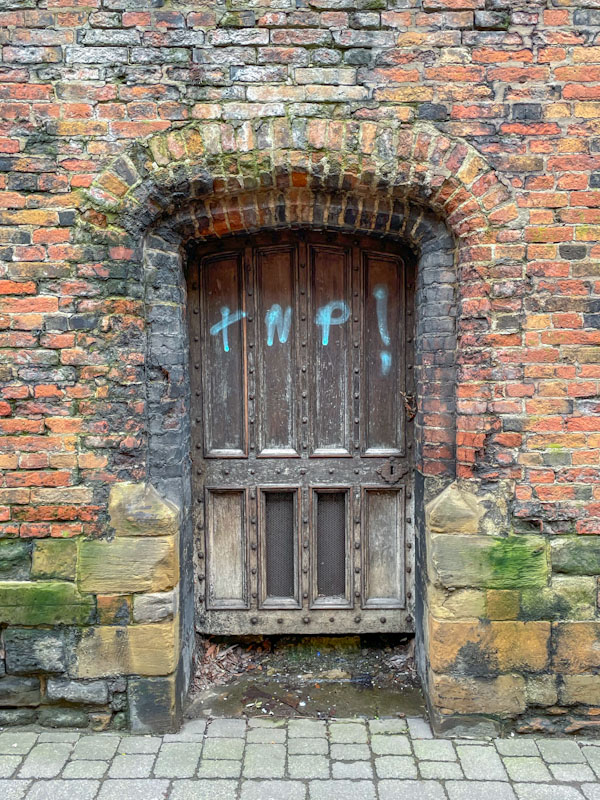 Old wooden door with studs in a brick wall, Nottingham, March 2024