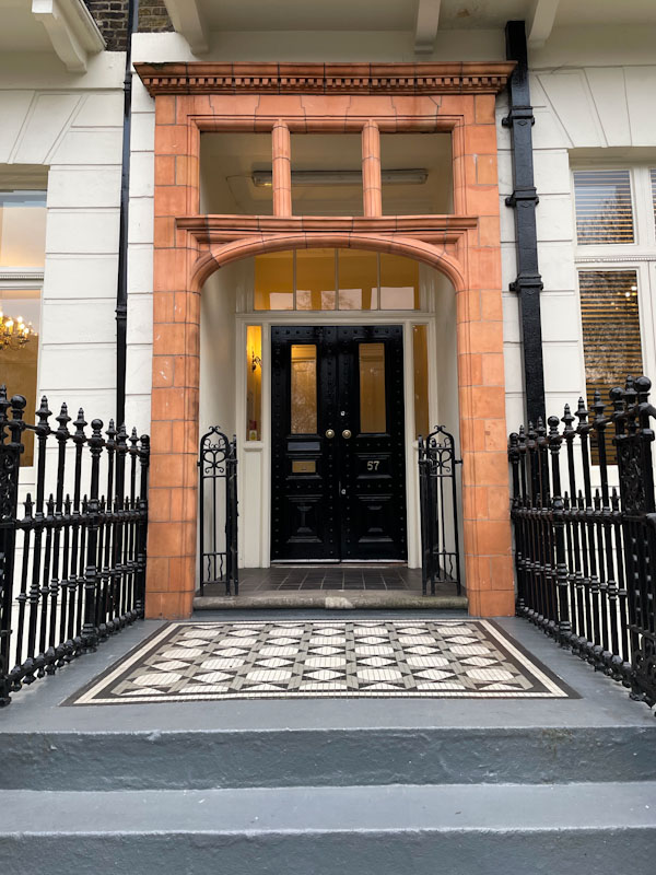 Stunning entrance with tiles, iron gates and red stone and modest black door , London, March 2024