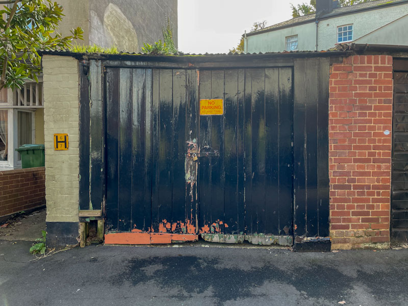 Black garage doors (once green and brick-red), Exeter, Devon, October 2023