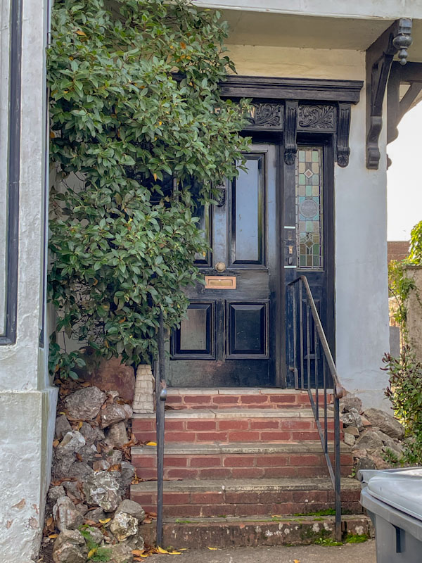 Black door with ornate wooden frame and stained-glass panel, Exeter, Devon, October 2023
