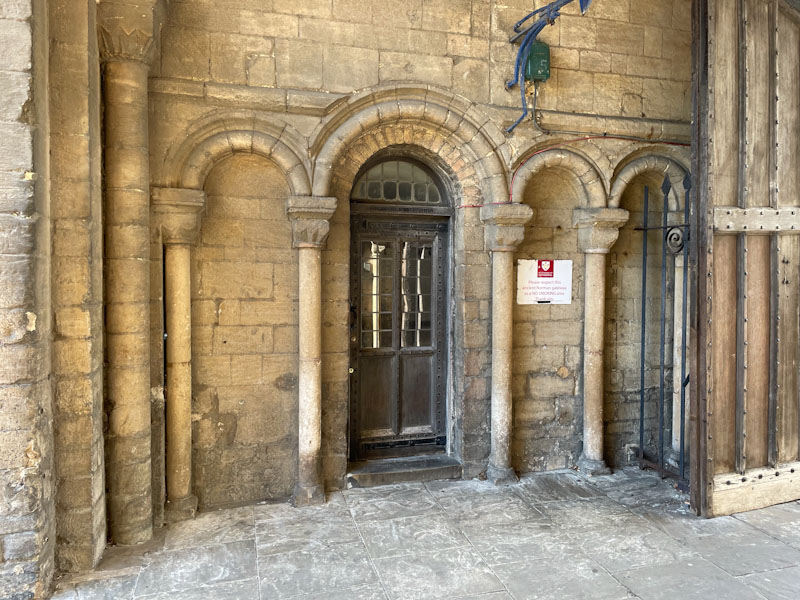 Norman arched doorway and wooden door. I foind the sign more offensive than the smoking it is there to advise against., Peterborough, Cambridgeshire, April 2024