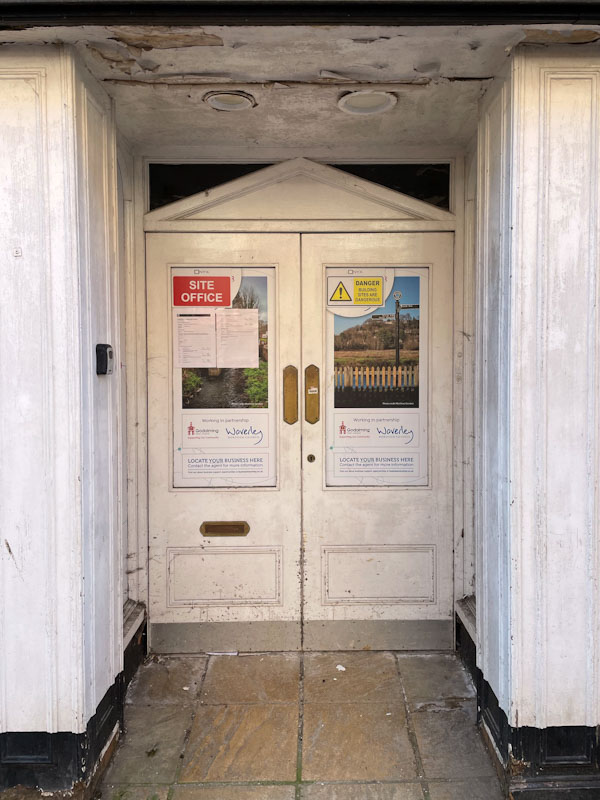Faux Regency door to a closed down retail outlet with a lot of notices, High Street, Godalming, Surrey, March 2025