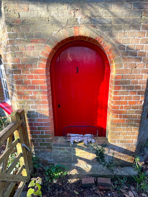Small red door with a flood wall built in front of it, Westbrook Road, Godalming, Surrey, March 2025