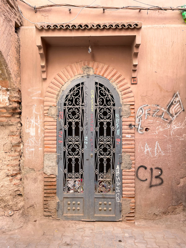 Arched iron door with litter piled up behind it,, Rue De La Bahia, Marrakesh, January 2025