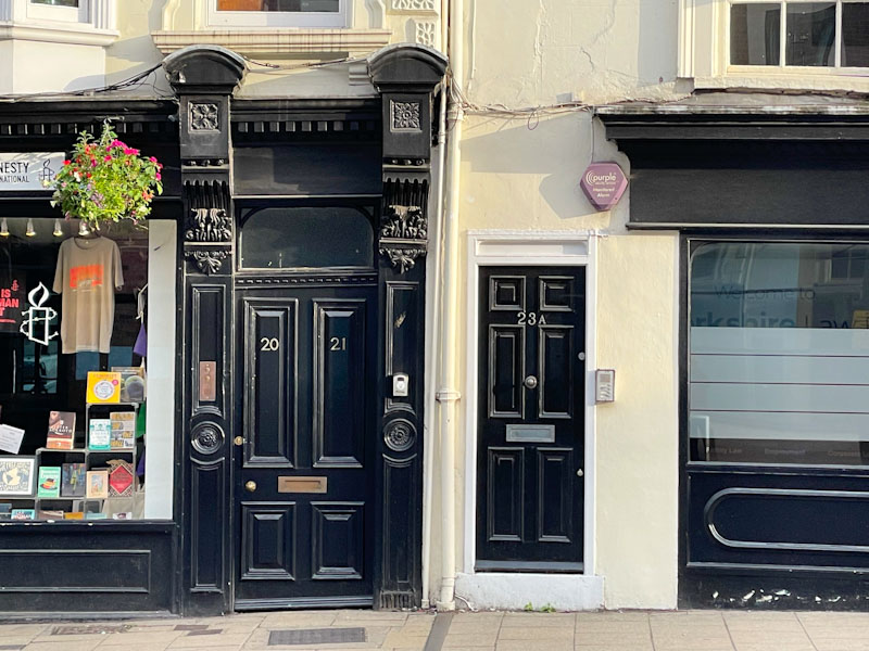 Two adjacent black doors each with very different surrounding styling, York, North Yorkshire, June 2024