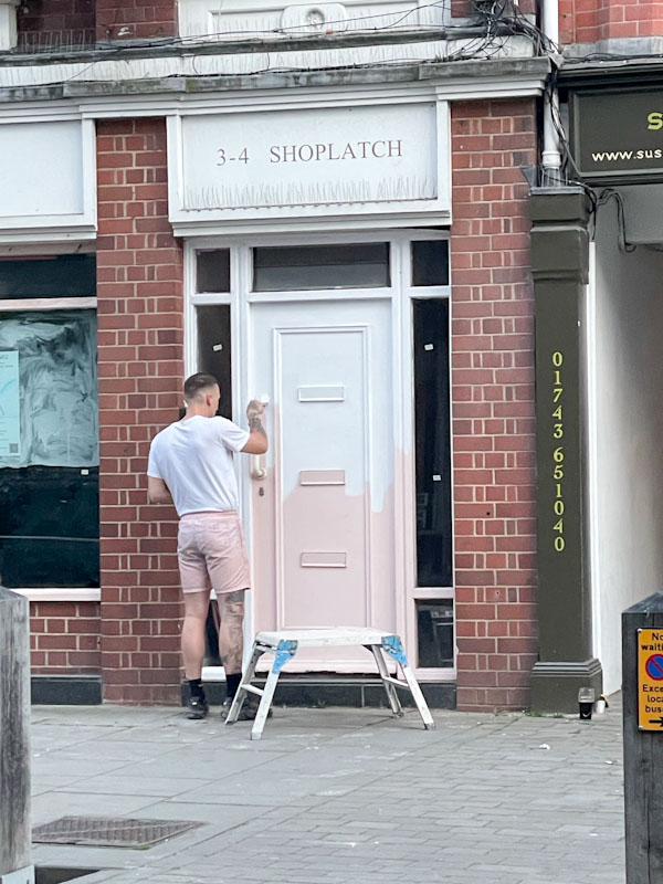 Serendipity - a man in white t-shirt and pink shorts matches the door he is painting perfectly, Shoplatch, Shrewsbury, Shropshire, England, April 2026