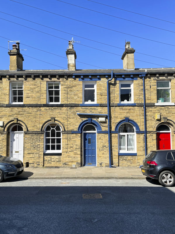 White, blue and red doors in a terrace, Titus Street, Saltaire, West Yorkshire, England, May 2025
