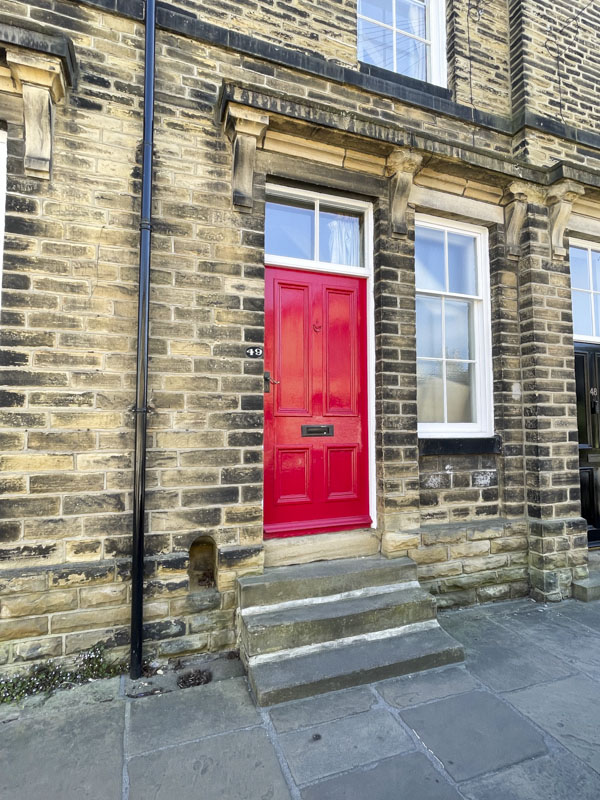Large red door and window above in end of terrace dwelling, Titus Street, Saltaire, West Yorkshire, England, May 2025