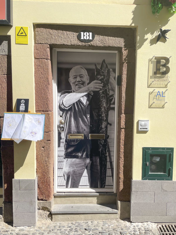 Door with a photograph of a man holding up a scabbard fish (local speciality), Rua de Santa Maria, Funchal, Madeira, September 2025